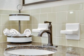 Ein Badezimmerwaschbecken mit modernem Wasserhahn, ein Handtuchhalter mit gefalteten Handtüchern und eine Seifenspender an der Wand.