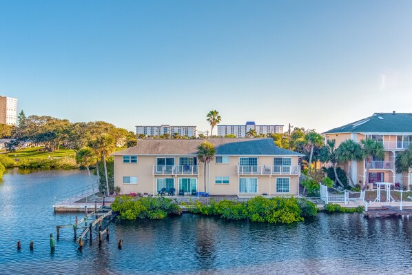 Ein Hotel am Wasser mit einer Anlegestelle, mehreren Balkonen und üppiger Bepflanzung.