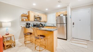 A compact kitchen with wooden cabinets, a microwave, a refrigerator, and a small island with two bar stools.
