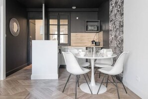 Une cuisine moderne équipée d’un four à micro-ondes, d’une machine à café et d’un plan de travail en bois. On y trouve également un coin repas avec une table et des chaises blanches.