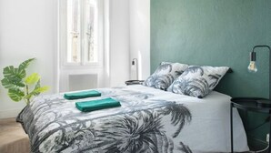 A bedroom with a bed, a green wall, a window, and a plant. - The Parrot 🦜 from La Rochelle 🐝 (La Rochelle)