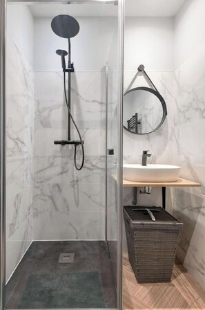 Une salle de bain moderne avec une douche à parois de verre, un miroir rond et un lavabo blanc.