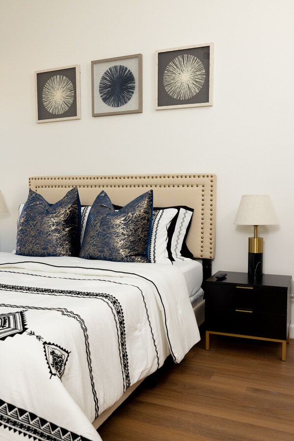 Un dormitorio ordenado con cama, mesitas de noche y una obra de arte colgada en la pared.