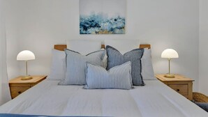 A bed with striped pillows, a wall-mounted abstract painting, and two bedside lamps.