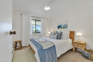 A bedroom with a bed, bedside tables, a window with curtains, a painting on the wall, and a door.
