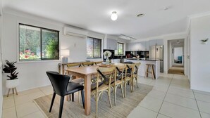 A modern kitchen with white cabinets, a dining area with a wooden table and chairs, and a view of the outdoors through large windows.