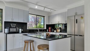 A modern kitchen with white cabinets, a central island with stools, stainless steel appliances, and a large window with a city view.