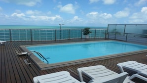 A pool area with a view of the ocean, deck chairs, and a potted plant. - Manaíra Palace Residence (João Pessoa)