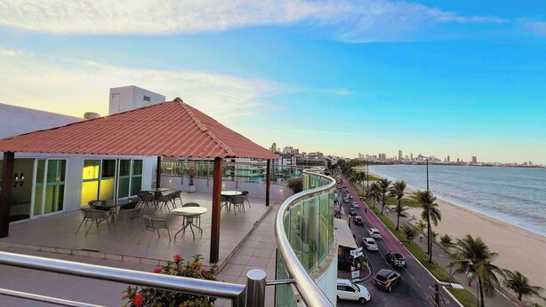 A rooftop terrace with outdoor seating, overlooking a beach and city skyline. - Manaíra Palace Residence (João Pessoa)
