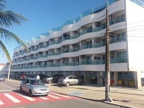 A multi-story building with balconies, a street in front, and parked cars.