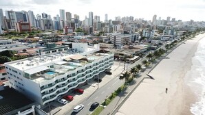 A coastal cityscape with modern buildings, a beach, and a road with parked cars. - Manaíra Palace Residence (João Pessoa)