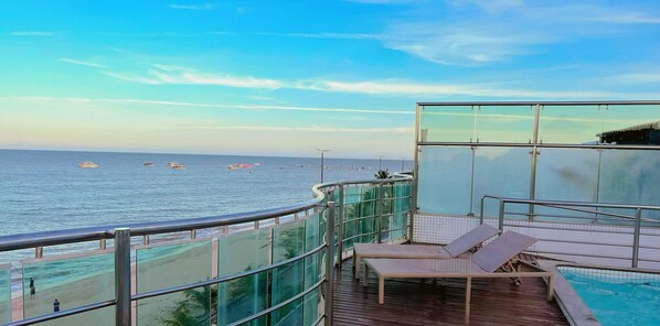 A balcony with a view of the sea, a pool, and a glass railing.