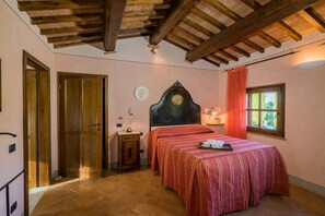 Un dormitorio con techo de madera, una cama con colcha estampada, una mesita de noche con lámpara y una ventana con cortinas.