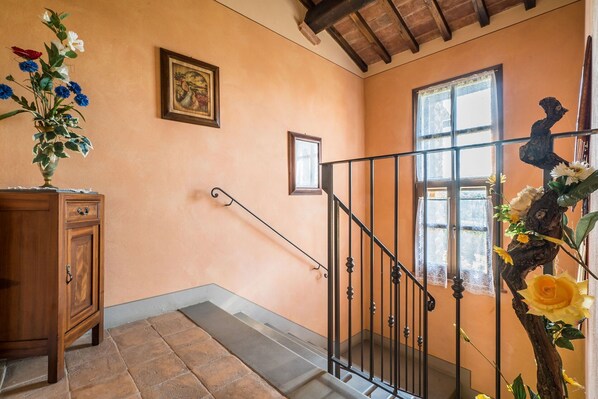Una escalera con barandilla de metal, un mueble de madera y un jarrón con flores a la izquierda.