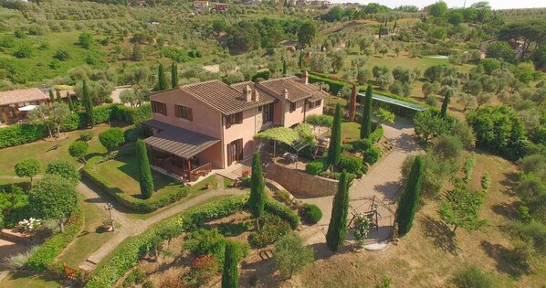 Una casa de dos pisos con un patio y jardín, rodeada de árboles y un paisaje montañoso.