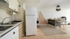 Eine moderne Küche mit Geschirrspüler, Kühlschrank und Spüle. Es gibt eine Essecke mit Tisch und Stühlen sowie eine kleine Sitzecke mit Sofa und Fernseher.