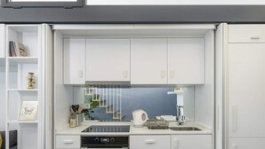 Een kleine keuken met witte kastjes, een ingebouwde oven en een spoelbak.