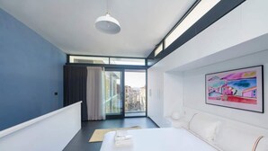 Een moderne hotelkamer met een groot bed, uitzicht op de stad door een schuifdeur en een schilderij aan de muur.