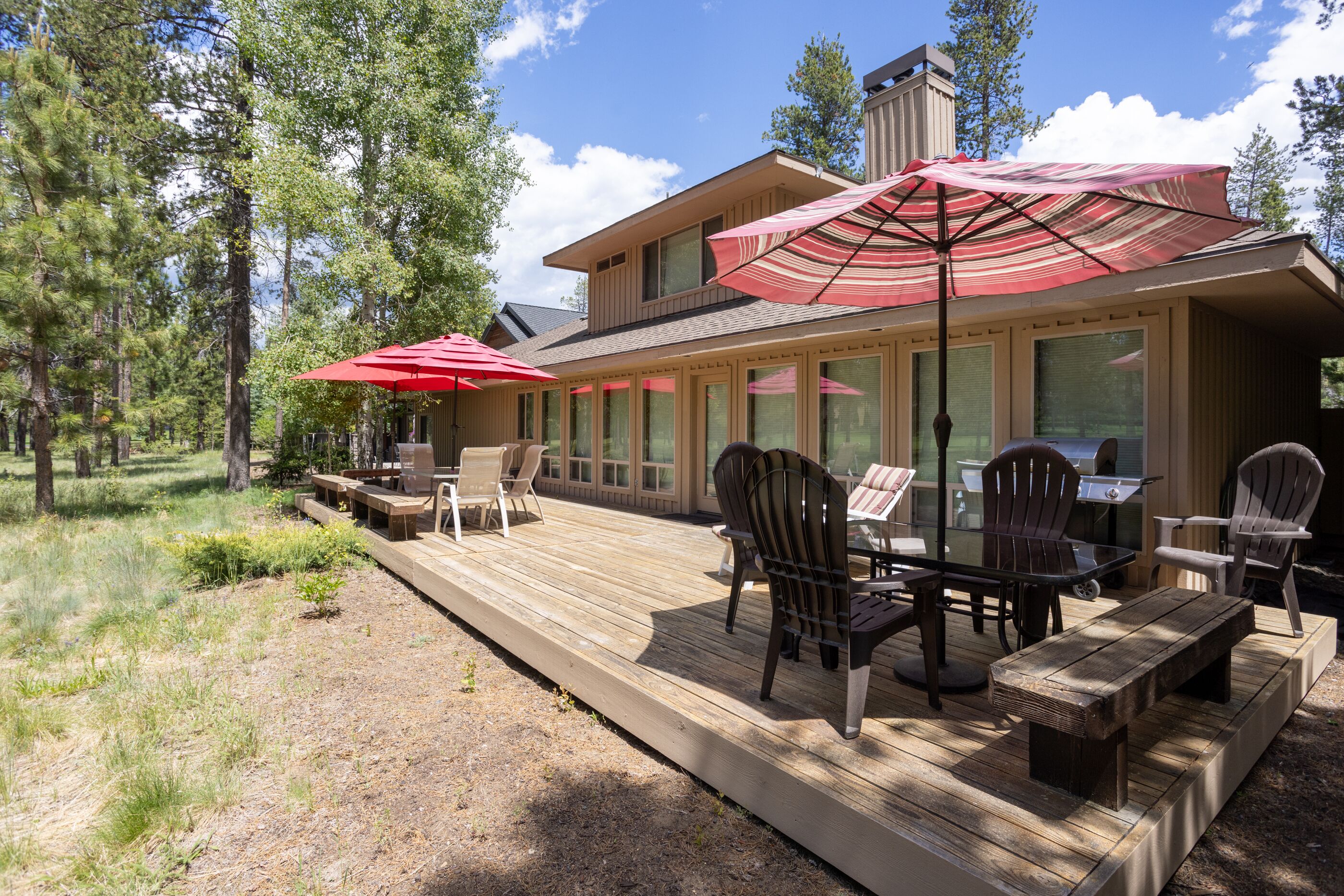 Une terrasse en bois, agrémentée de meubles d’extérieur et de parasols, entourée d’arbres.
