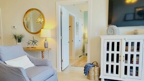 Een woonkamer met een gestreept bankje, een ronde spiegel, een lamp en een witte kast met glazen deuren.