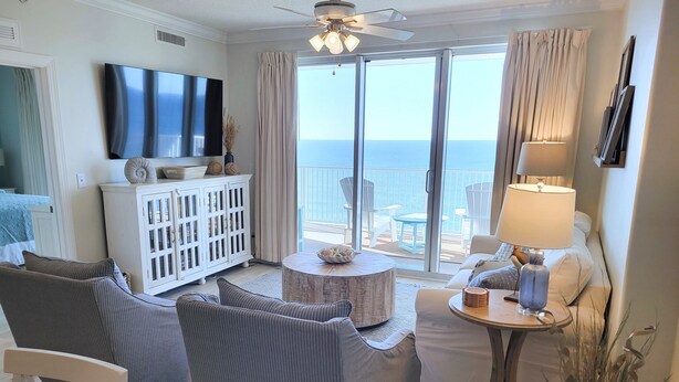 Een woonkamer met een grote televisie, een wit kastje, een ronde salontafel en uitzicht op de oceaan.