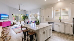 A modern kitchen with white cabinets, a large island, and a dining area with bar stools. - Beach + Heated Pool + Game Room + 2 King Suites (Naples)