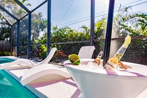 Escena junto a la piscina con una silla lounge blanca, un bol de cristal con una botella de Corona y una cuña de limón.