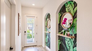 A hallway with a white door, a wooden floor, and a wall with a tropical leaf pattern. - Beach + Heated Pool + Game Room + 2 King Suites (Naples)