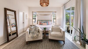 A bedroom with a large bed, two armchairs, a mirror, and a hanging light fixture. - Beach + Heated Pool + Game Room + 2 King Suites (Naples)