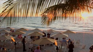Un espace extérieur aménagé pour les repas, avec des tables et des parasols, offrant une vue sur l’océan au coucher du soleil.