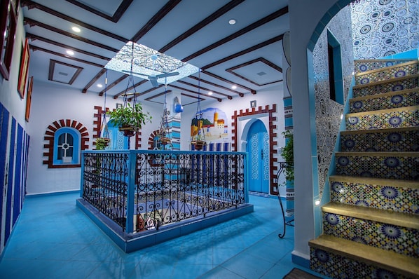 A room with a blue floor, a decorative ceiling fan, a patterned staircase, and a blue door with a white arch.