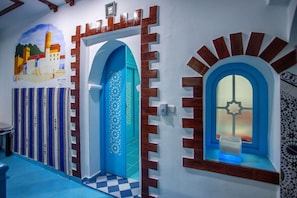 A hallway with a blue door, a blue window with a star design, and a mural of a building on the wall.