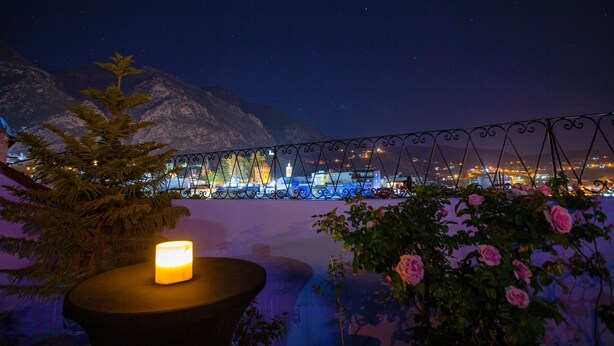 Vista nocturna de un balcón con una vela, una montaña al fondo y luces de la ciudad.