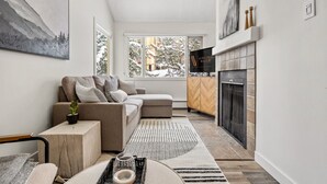 A modern living room with a sofa, a fireplace, and a large window. - Kauhoolio | Toby | Pool | Hot Tub | Sauna (Panorama)