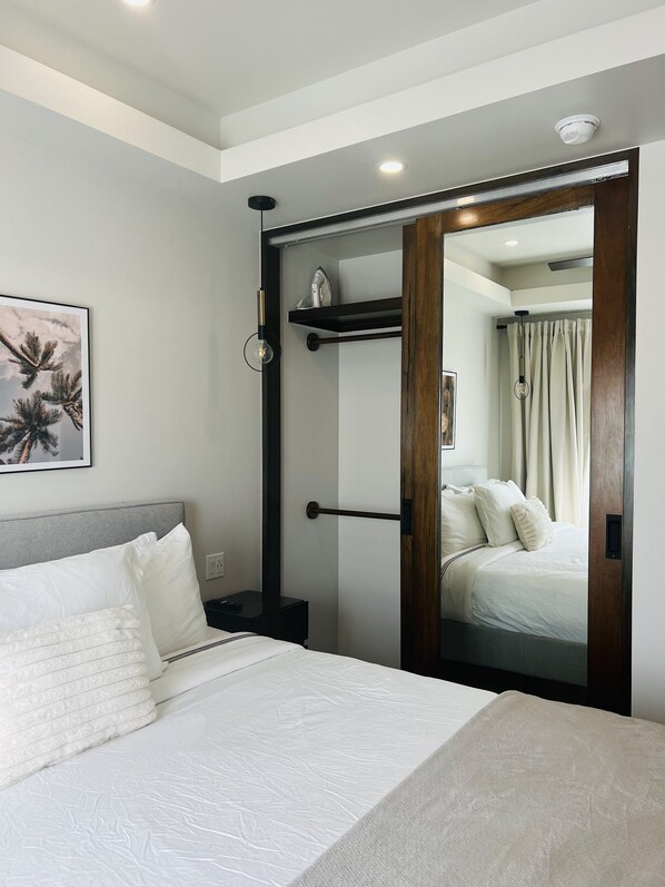 Una habitación de hotel moderna con una cama, una mesita de noche, un estante montado en la pared, una puerta con espejo y una lámpara en el techo.