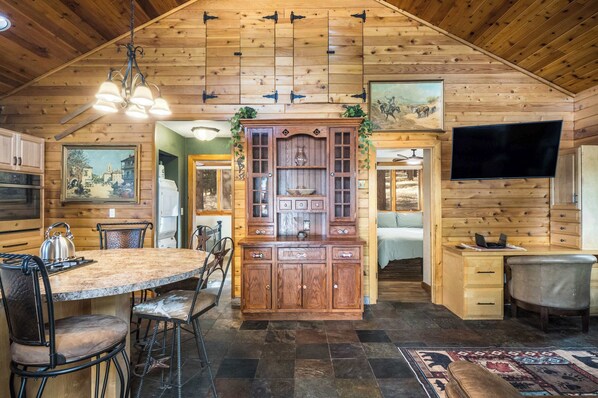 A wooden interior with a kitchen area, dining table, and a TV mounted on the wall. - Coleman Velo - Secluded Rustic Cabin (Angel Fire)