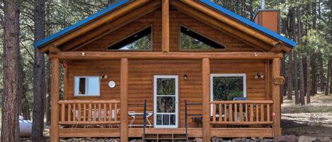 Eine Holzhütte mit blauem Dach, zwei Fenstern, einer Tür und einer Veranda.