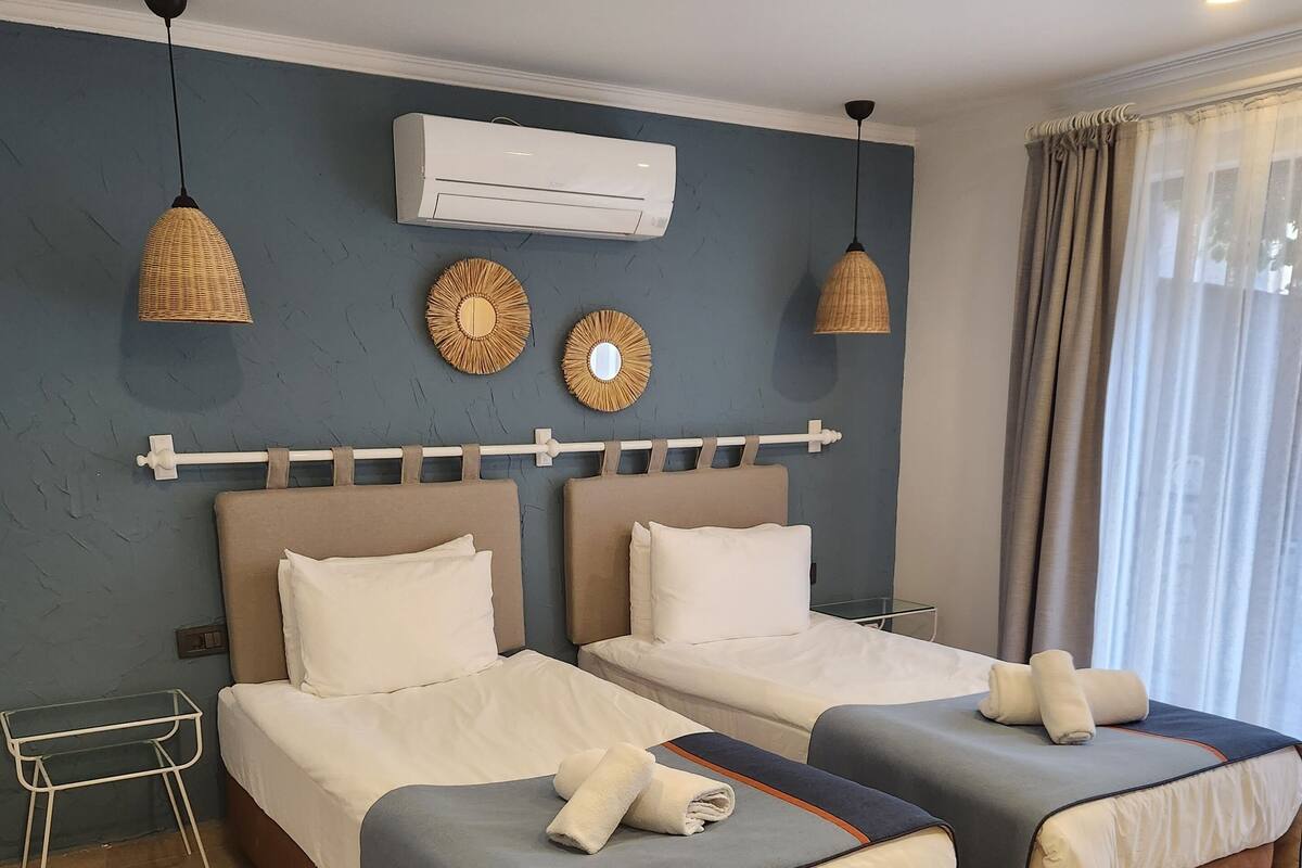 Een hotelkamer met twee bedden, een tafeltje en een raam met gordijnen.