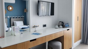 Ein Hotelzimmer mit weißem Schreibtisch, einem großen Spiegel, einem Flachbildfernseher, einem Bett mit blauer Kopfteil und einem Kleiderschrank.
