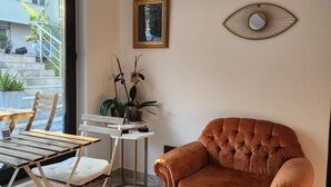 Ein Wohnzimmer mit einem braunen Sessel, einem weißen Tisch mit Stühlen, einem kleinen Beistelltisch mit einer Pflanze und einem gerahmten Bild an der Wand.
