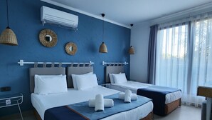 Ein Hotelzimmer mit zwei Betten, einem großen Fenster mit Vorhängen, einer Wand-Klimaanlage und dekorativen Wandspiegeln.