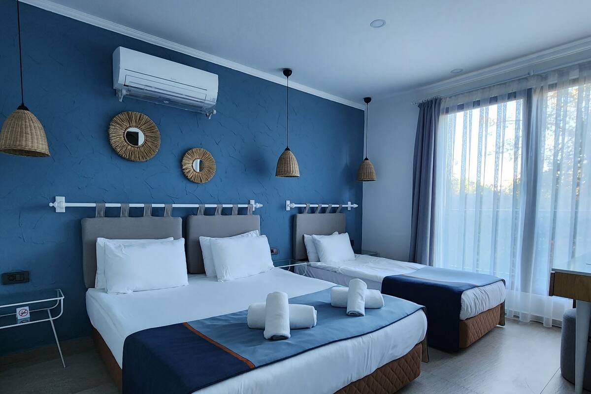 Een hotelkamer met twee bedden, een groot raam met gordijnen, een luchtverkoeler aan de muur en decoratieve spiegelwanden.
