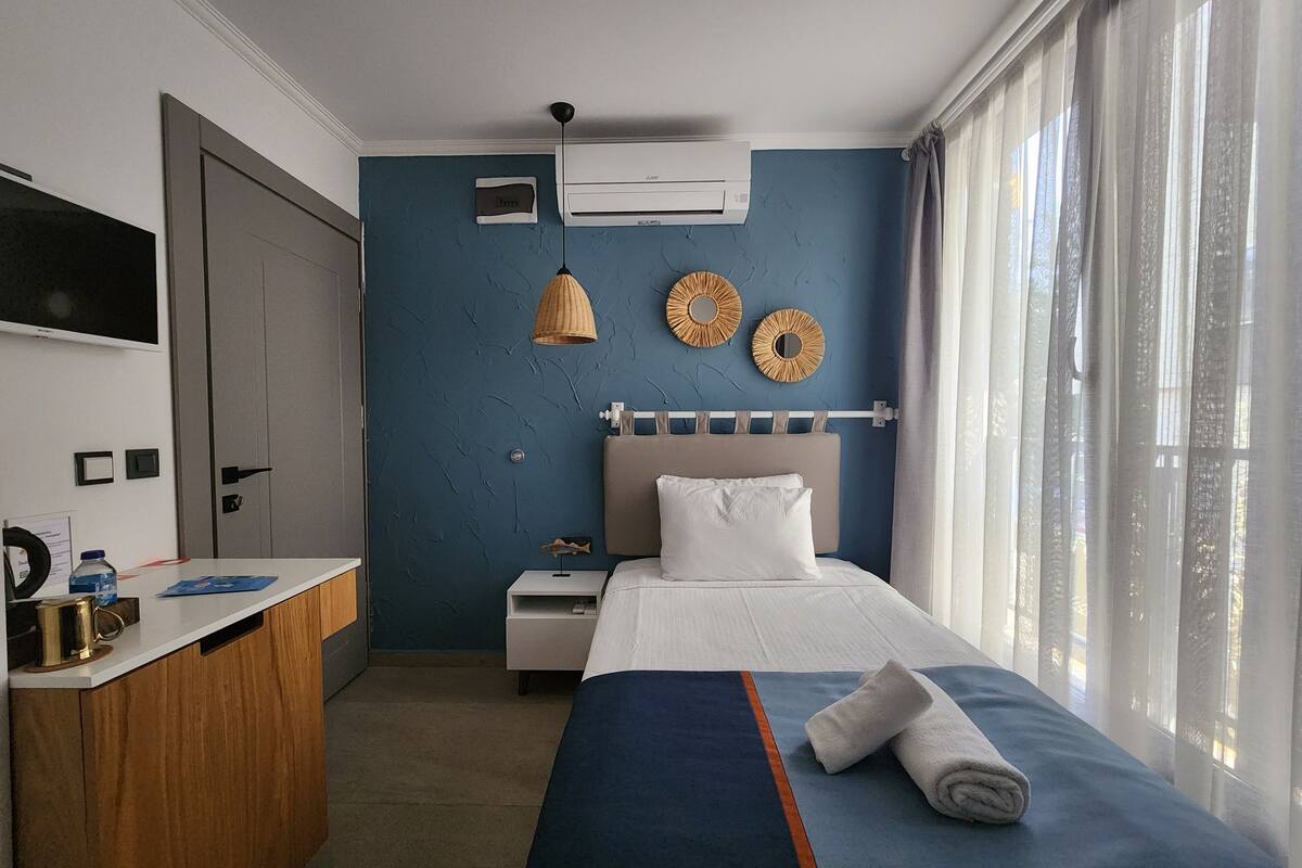 Een hotelkamer met een bed, een bureau, een airconditioner en een raam met gordijnen.