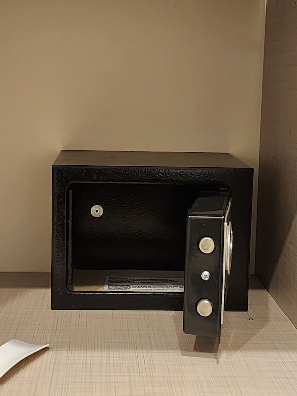 Un coffre-fort noir, de style ancien, doté d’une poignée et de deux serrures apparentes, placé contre un mur de couleur beige.