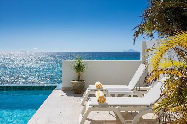 Ein Poolbereich mit Liegestühlen und Blick aufs Meer.