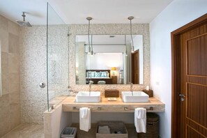 Une salle de bain moderne avec une douche à parois de verre, un grand miroir, deux lavabos et une porte en bois.