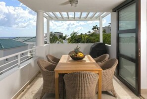 Un balcon avec des fauteuils en osier, une table en bois et un saladier rempli de fruits.