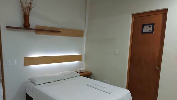 Un letto ben rifatto con lenzuola bianche, un comodino con una lampada e una testiera in legno.