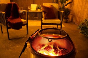 A grill with a mesh cover and a fire burning inside, placed on a concrete surface.