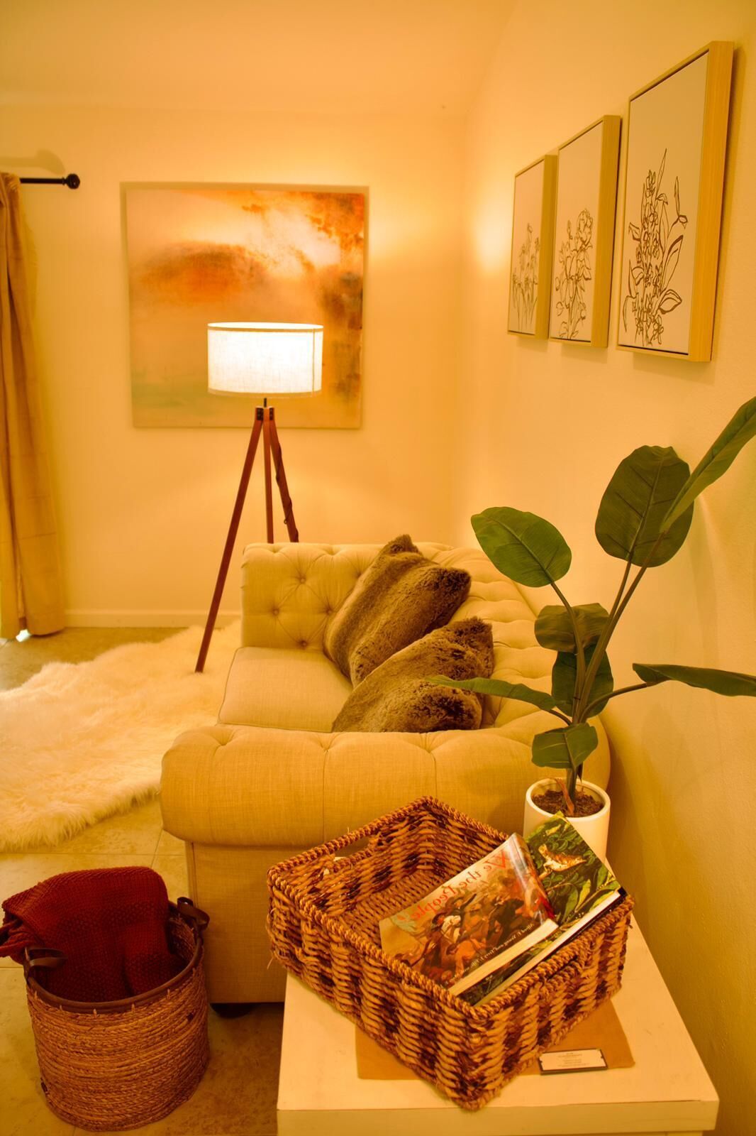 A cozy living room with a yellow sofa, a floor lamp, a large painting, and a potted plant.
